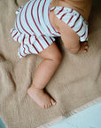 Baby wearing white swimsuit with red stripes and ruffles