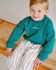 child wearing green fleece sweatshirt with striped pants
