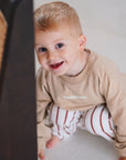 child wearing beige fleece sweatshirt with striped pants close up