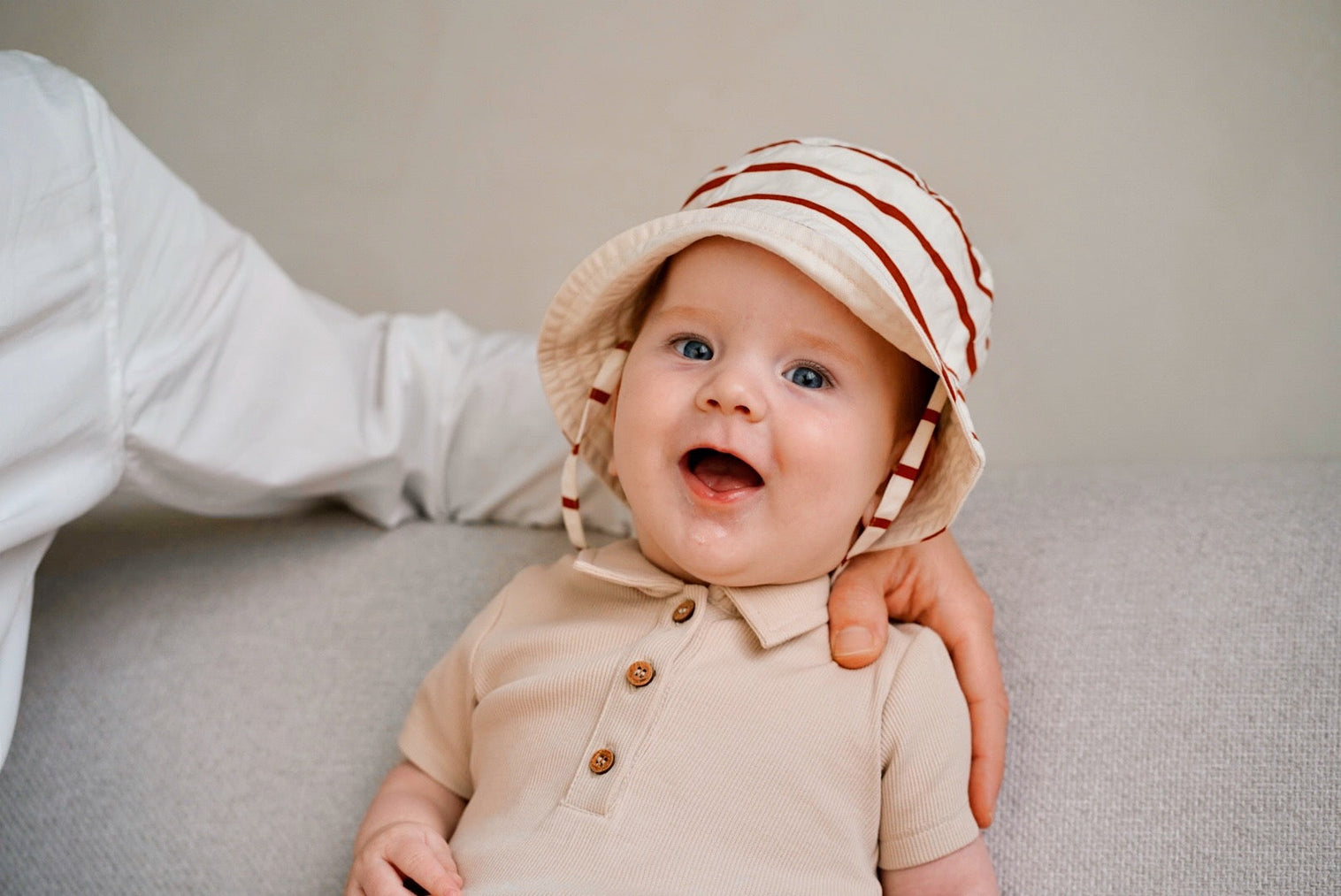 baby wearing beige rib romper and matching hat smiling