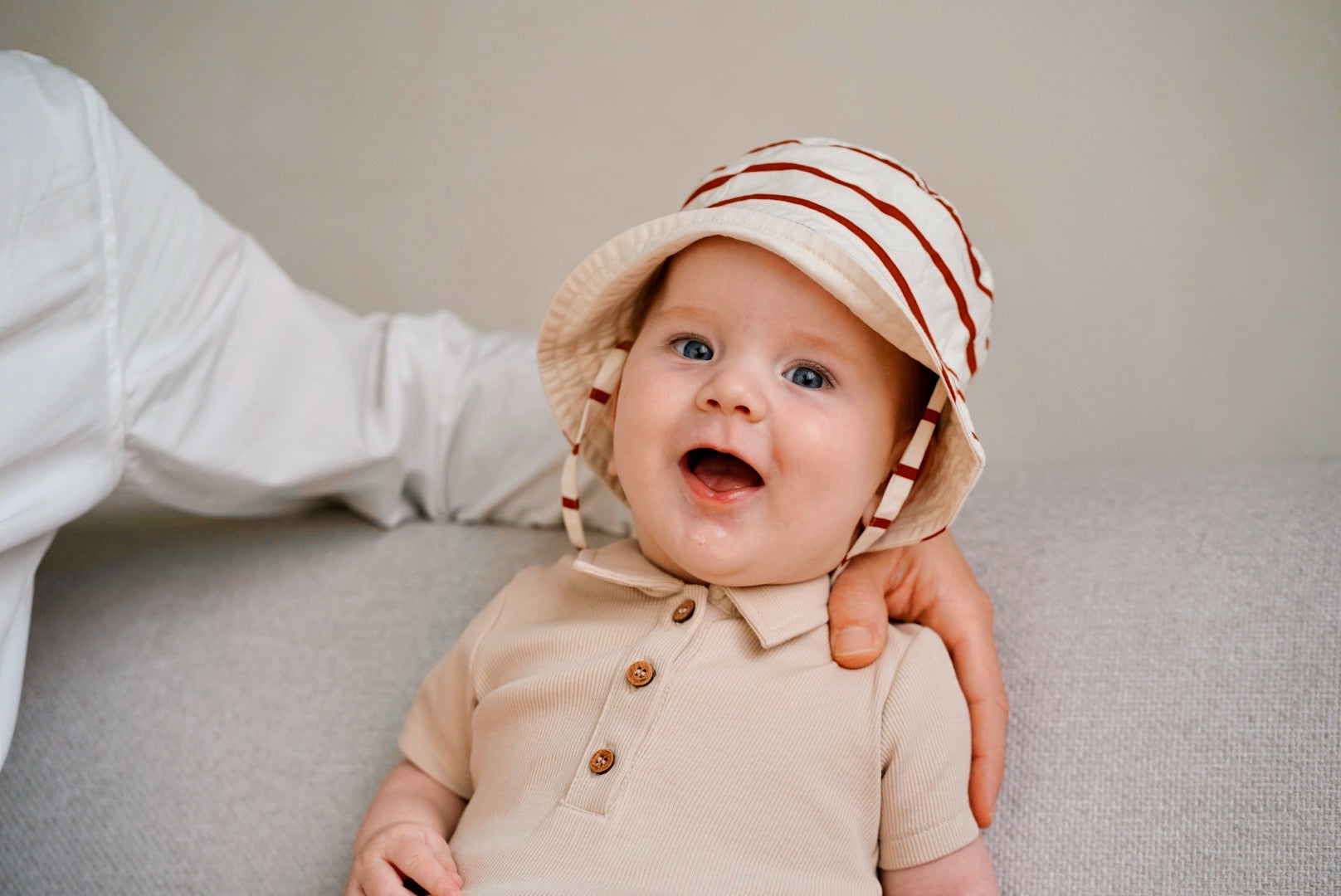 baby wearing beige rib romper and matching hat smiling