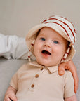 baby wearing beige rib romper and matching hat smiling