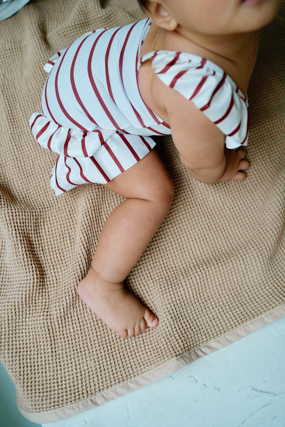 Baby wearing white swimsuit with red stripes and ruffles
