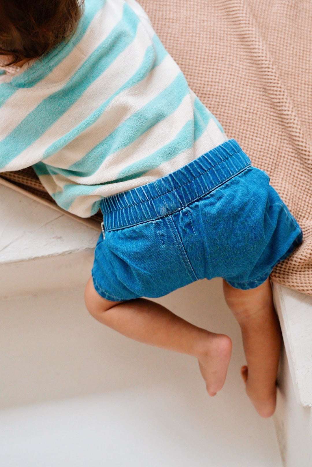 Child wearing blue cotton denim shorts with elastic waistband back view