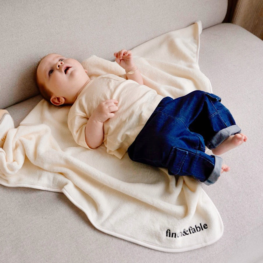 Child wearing cream white muslin short sleeve t-shirt with wooden buttons while lying down