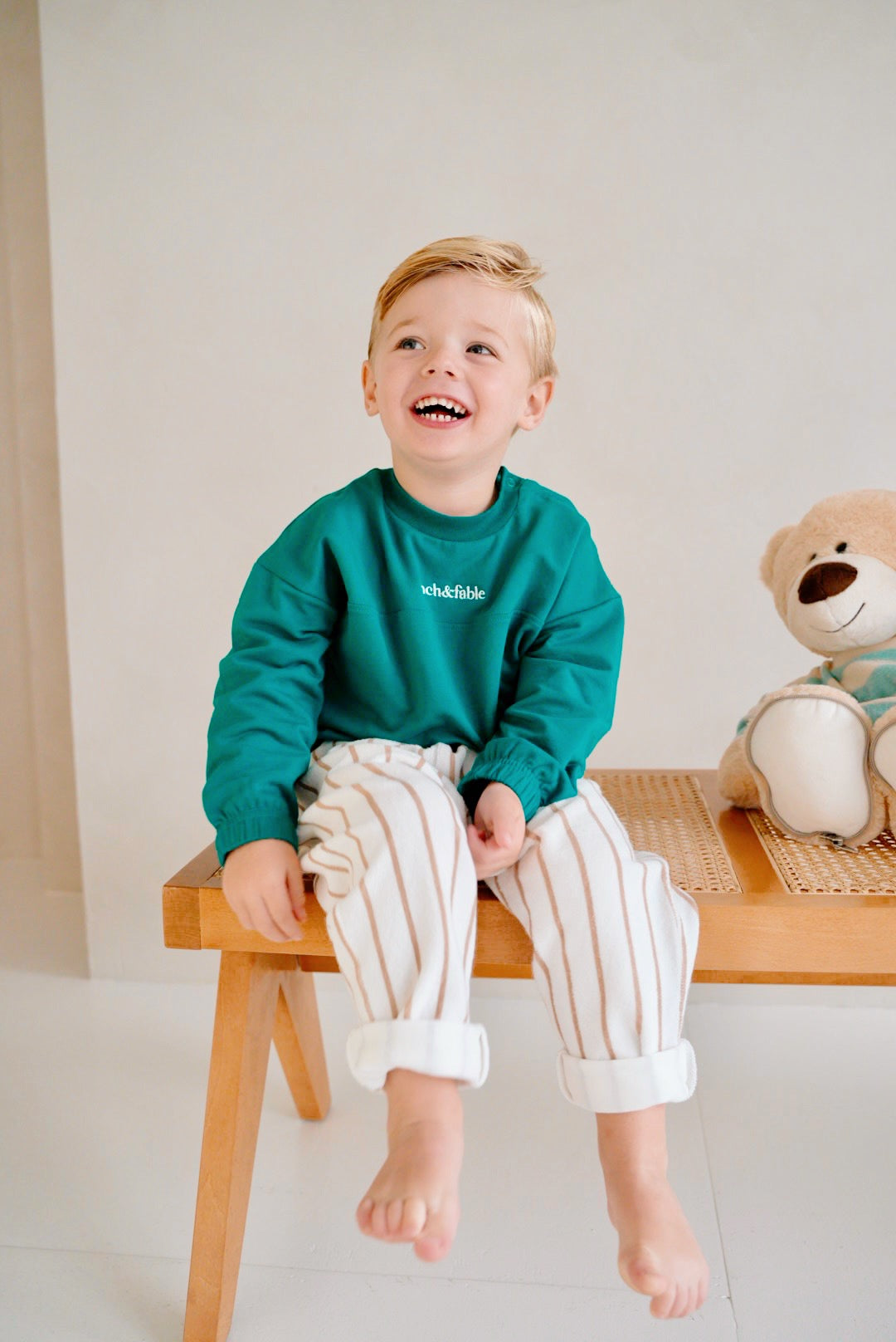 child wearing green fleece sweatshirt with striped pants front view