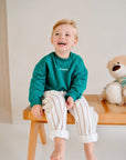 child wearing green fleece sweatshirt with striped pants front view