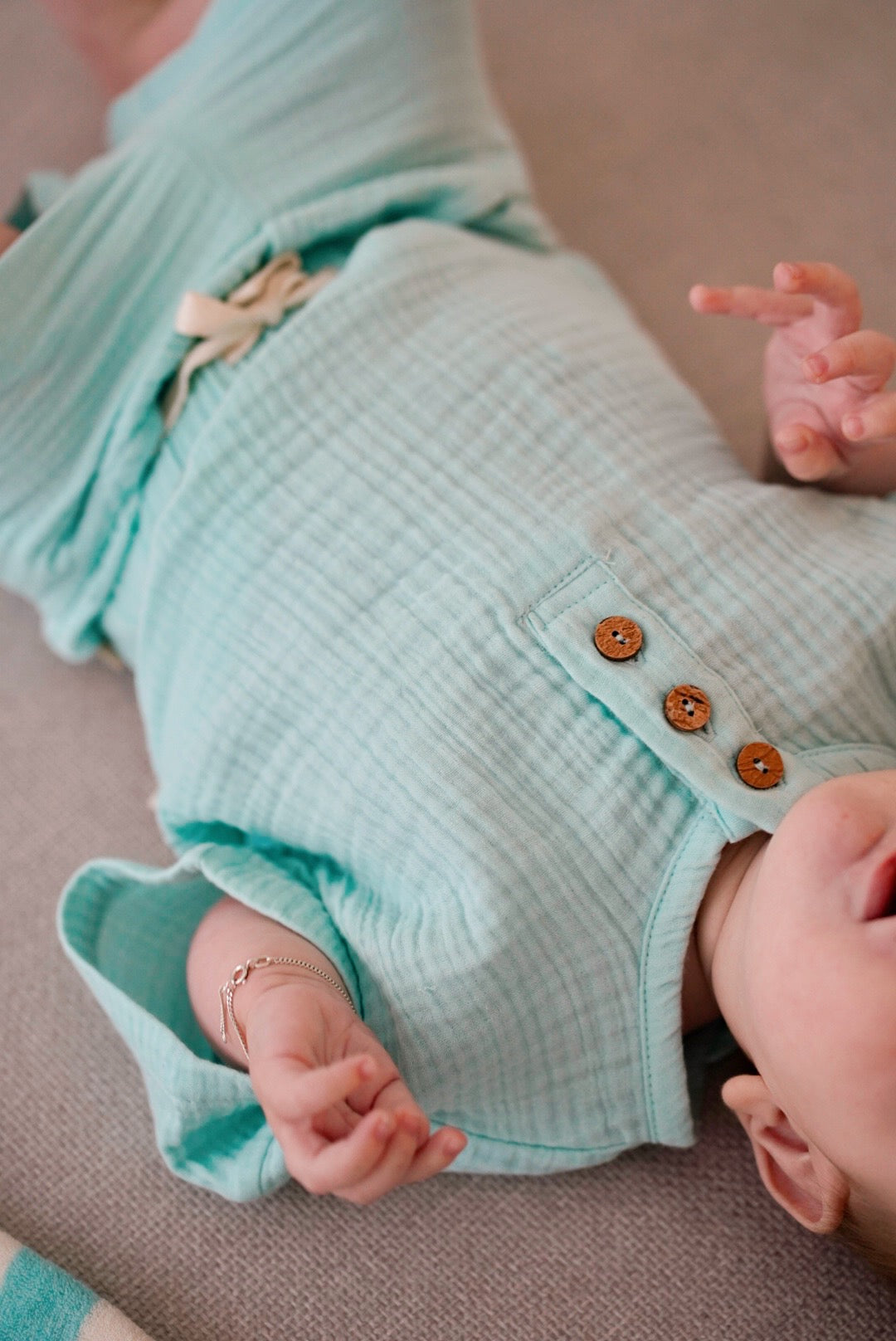 Child wearing light blue muslin short sleeve t-shirt with wooden buttons while lying down
