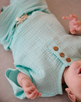 Child wearing light blue muslin short sleeve t-shirt with wooden buttons while lying down
