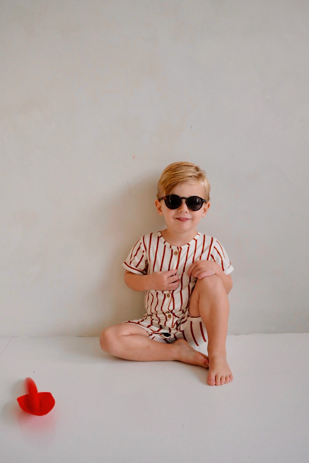 child wearing white cotton playsuit with red stripes while sitting