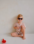 child wearing white cotton playsuit with red stripes while sitting