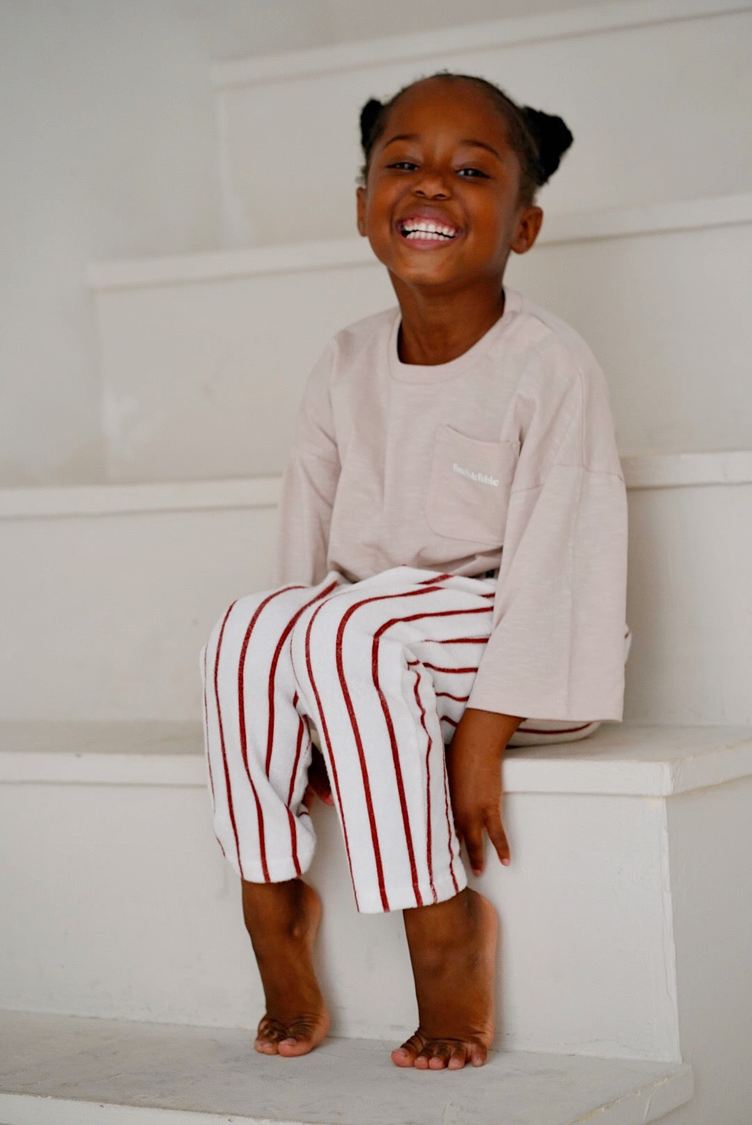 Child wearing white cotton terry pants with red stripes while sitting