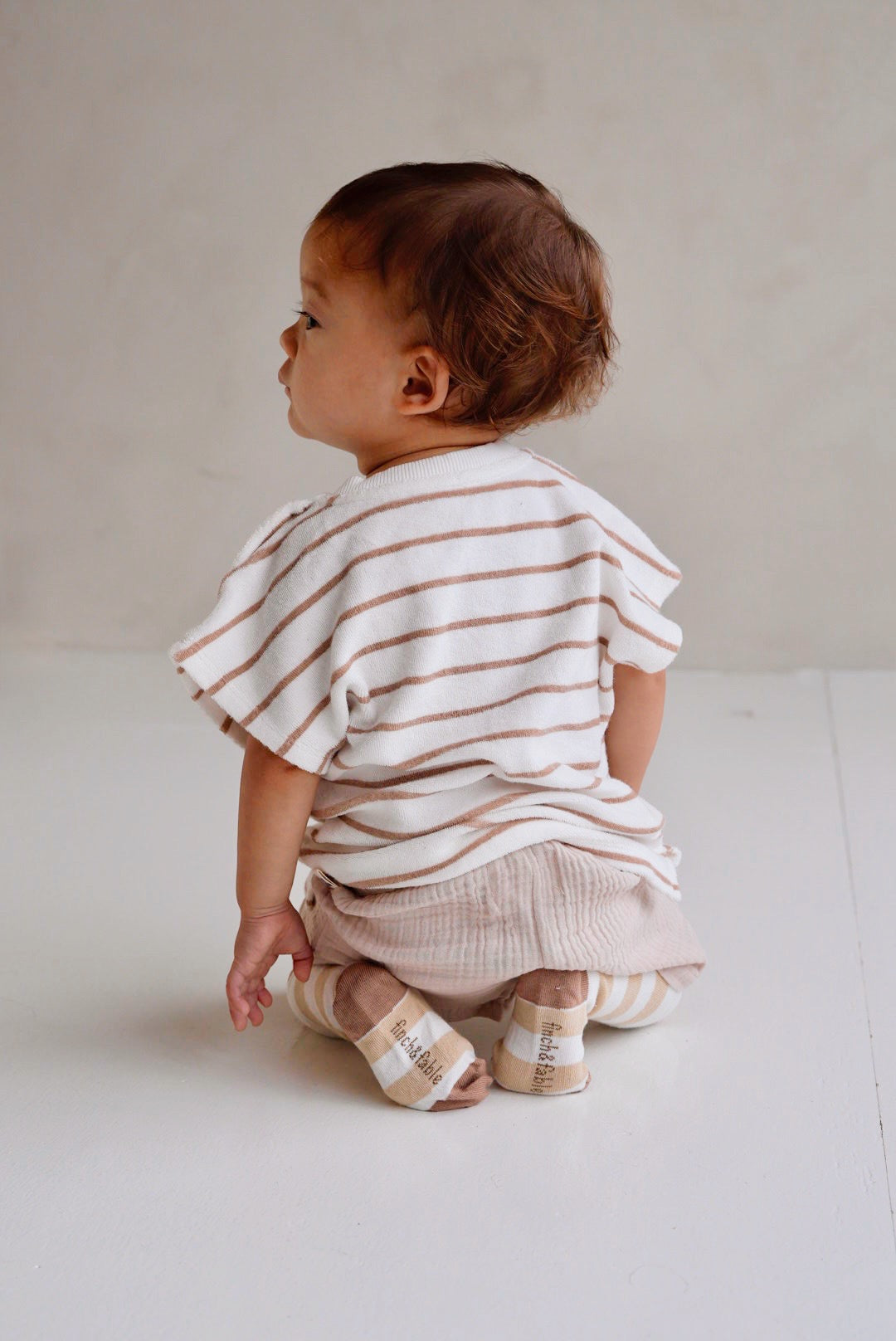 Toddler wearing beige striped cotton terry shirt with wooden buttons back view